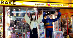 女子和機器人雕像在設有玻璃展示櫃的動漫店外舉起拳頭。 — 可愛動漫頭貼 GIF 壁紙