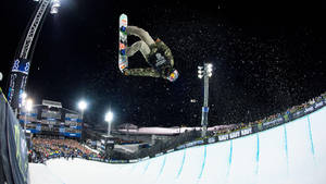 滑雪板運動員在夜間雪地活動中，在觀眾和燈光下於空中表演技巧。 — X Games 壁紙