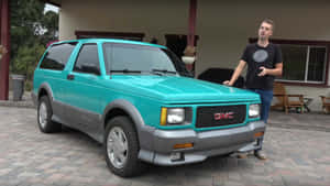 男子站在磚砌庭院上的青綠色GMC Typhoon SUV旁。 — 1920x1080 壁紙