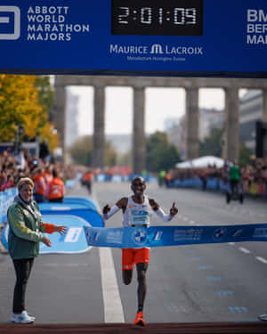 一名男性跑者衝過BMW柏林馬拉松的終點線，露出勝利的笑容。 — Running 壁紙