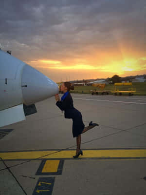 空服員在日落時分於停機坪親吻飛機機頭 — 夕陽天空 壁紙