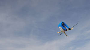 穿藍色外套的滑雪者在空中，背景為多雲的天空 — 運動 壁紙
