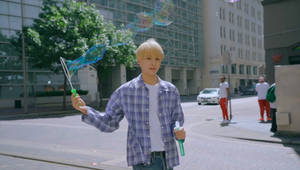 年輕男子在陽光明媚的人行道上吹出彩色泡泡。 — Nct 127 壁紙