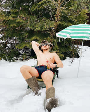 穿著泳褲和毛帽的男子在雪地上放鬆，有飲料和傘。 — 雪人 壁紙