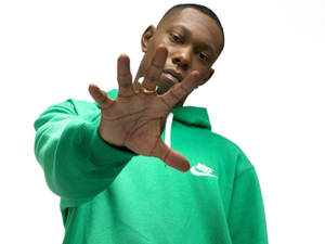 穿綠色連帽衫的男子表情嚴肅地伸出手。 — Skepta 壁紙