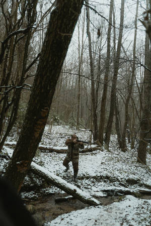 一名穿著迷彩裝備的獵人在白雪皚皚的冬季森林中持步槍。 — 狩獵 GIF 壁紙