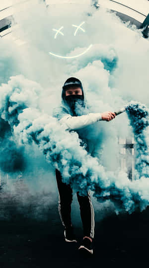 穿著連帽衫和口罩的人釋放出藍色煙霧，上方有一個發光的笑臉。 — 藍色煙霧 壁紙