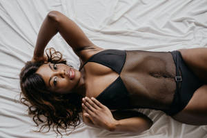 一名穿著黑色內衣的女人躺在白色床上看著鏡頭。 — 模特兒 壁紙