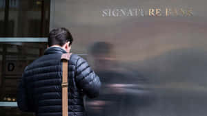 穿著黑色羽絨外套的男子站在 Signature Bank 大樓前，倒影模糊。 — 外灘群島 壁紙