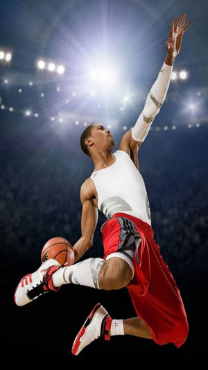 身穿白色球衣和紅色短褲的運動員在體育館燈光下持籃球跳躍。