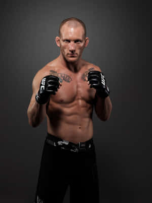 一名赤裸上身的男性拳手，戴著黑色UFC手套和穿著黑色短褲，擺出戰鬥姿勢。 — 終極格鬥冠軍賽 壁紙