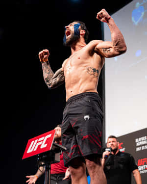 UFC拳手在舞台上高舉拳頭慶祝勝利。 — 運動 壁紙