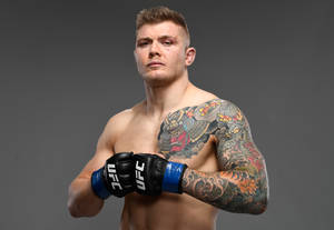 一名有紋身的男性UFC戰士戴著手套在攝影棚中嚴肅地擺姿勢。 — 運動 壁紙