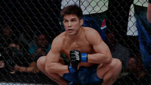 一名男性MMA戰士蹲在籠內，穿著藍色短褲和黑色手套。 — 終極格鬥冠軍賽 壁紙