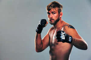 一名赤裸上身的男性MMA拳手戴著黑色UFC手套，在工作室中舉起拳頭擺姿勢。 — 終極格鬥冠軍賽 壁紙