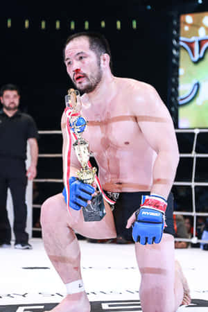 MMA拳手在八角籠中獲勝後跪地手持冠軍獎盃 — 庫洛魔法使 壁紙