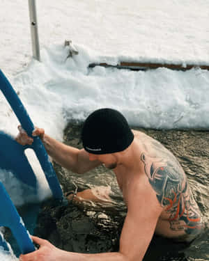 有刺青的男子在白雪皚皚的冬日景色中用藍色梯子從冰水中爬出。 — 游泳 壁紙