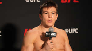 赤裸上身的UFC拳手在記者會上對著麥克風說話。 — 1600x900 壁紙