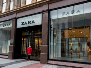 身穿紅色外套的人站在Zara店鋪入口的城市人行道上。 — Zara 壁紙