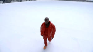 一名身穿紅色雪衣的男子在深雪中行走。 — 肯伊·威斯特 壁紙