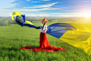 身穿傳統服飾的女子在日出時分的綠色田野中手持烏克蘭國旗。 — 烏克蘭 壁紙