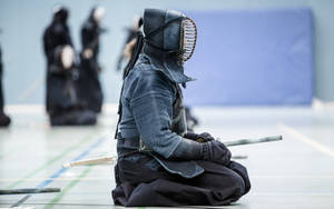 全副武裝的劍士在道場中手持竹劍跪地。 — 運動 壁紙