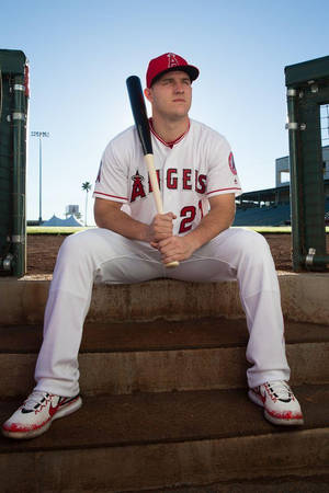 身穿天使隊球衣的棒球運動員坐在體育場階梯上手持球棒。 — Mike Trout 壁紙