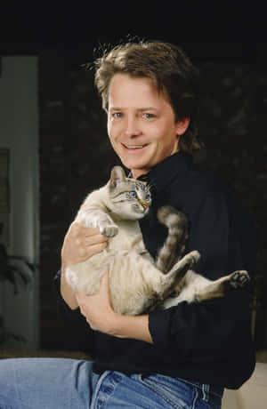 男子在室內抱著一隻藍眼睛的灰色虎斑貓 — 狐狸 GIF 壁紙
