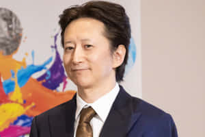 身穿西裝打領帶的男子對著鏡頭微笑，身後是色彩繽紛的抽象藝術。 — 春野櫻 壁紙