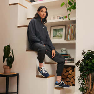 身穿運動服的女性坐在現代樓梯上，旁邊有植物和黑膠唱片。 — New Balance 壁紙
