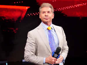 身穿西裝的WWE播音員在紅色燈光的舞台上手持麥克風。 — WWE GIF 壁紙