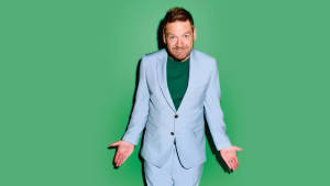 身穿淺藍色西裝和綠色襯衫的男子在綠色背景前張開雙臂擺姿勢。 — 好萊塢 壁紙