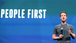 男子在舞台上對著麥克風說話，身後有「PEOPLE FIRST」文字。 — 馬克·祖克柏 壁紙