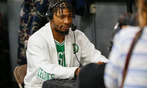 身穿Celtics連帽衫並佩戴耳機的籃球運動員接受媒體採訪。 — 馬庫斯·史馬特 壁紙