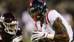 美式足球員帶球奔跑，防守球員在球場燈光下逼近。 — Dk Metcalf 壁紙