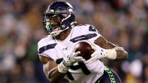 西雅圖海鷹隊美式足球員在夜間比賽中帶球奔跑。 — Dk Metcalf 壁紙