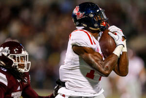 美式足球員在夜間比賽中接球，防守球員在附近。 — Dk Metcalf 壁紙