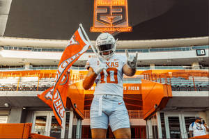 德州足球運動員在體育場揮舞旗幟並做出搖滾手勢。 — 大學美式足球 壁紙