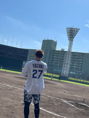 棒球選手穿著Suzuki 27號球衣，在陽光明媚的球場上面對體育場。 — 運動 壁紙