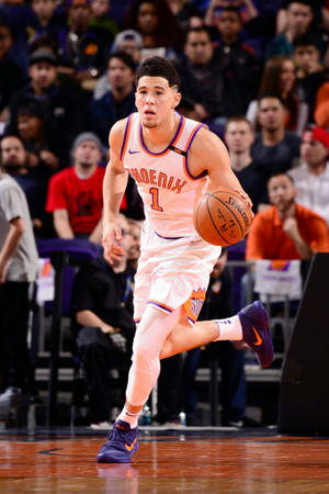 籃球運動員在比賽中運球，背景有觀眾。 — Devin Booker 壁紙