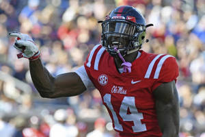 身穿紅色 Ole Miss 14 號球衣的足球運動員舉起拳頭慶祝。 — Dk Metcalf 壁紙