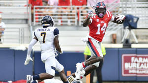 14號足球員躍起接球，同時被防守球員追趕。 — Dk Metcalf 壁紙