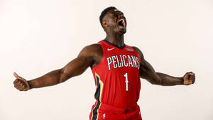 身穿紅色Pelicans球衣的籃球運動員張開雙臂慶祝勝利。 — 錫安·威廉森 壁紙