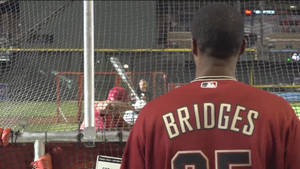 身穿紅色球衣的棒球選手 bridges 在打擊籠前與投手對峙。 — 運動 壁紙