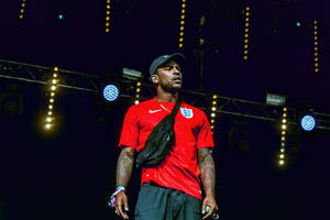 身穿紅色英格蘭球衣的男子在舞台燈光下的舞台上 — Skepta 壁紙