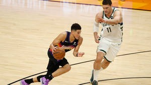 籃球運動員在比賽中運球越過防守球員 — Devin Booker 壁紙