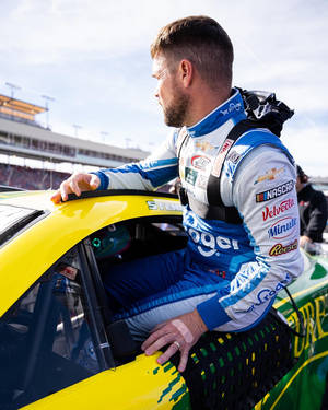 NASCAR車手身穿賽車服從黃色賽車中探出身子在賽道上 — 跑車 壁紙