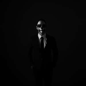 在昏暗工作室燈光下，身穿西裝、臉上繪有骷髏圖案的男子 — 暗黑風格 壁紙