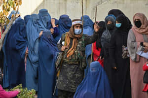 身穿迷彩服的士兵在戶外牆邊引導一群戴面紗的女性。 — 阿富汗 壁紙