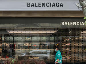 身穿青綠色襯衫和口罩的人走過 Balenciaga 商店，玻璃窗關閉。 — 巴黎世家 壁紙